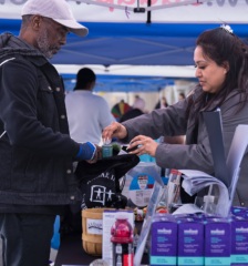 A woman places a bottle of hand sanitizer into a man's bag at a community event outdoors.